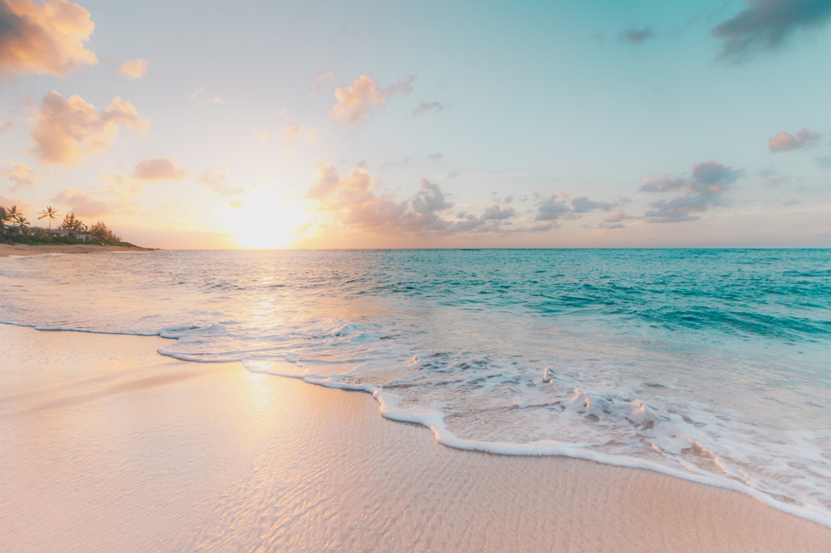 Sunrise over a calm sandy beach with gentle waves and golden light